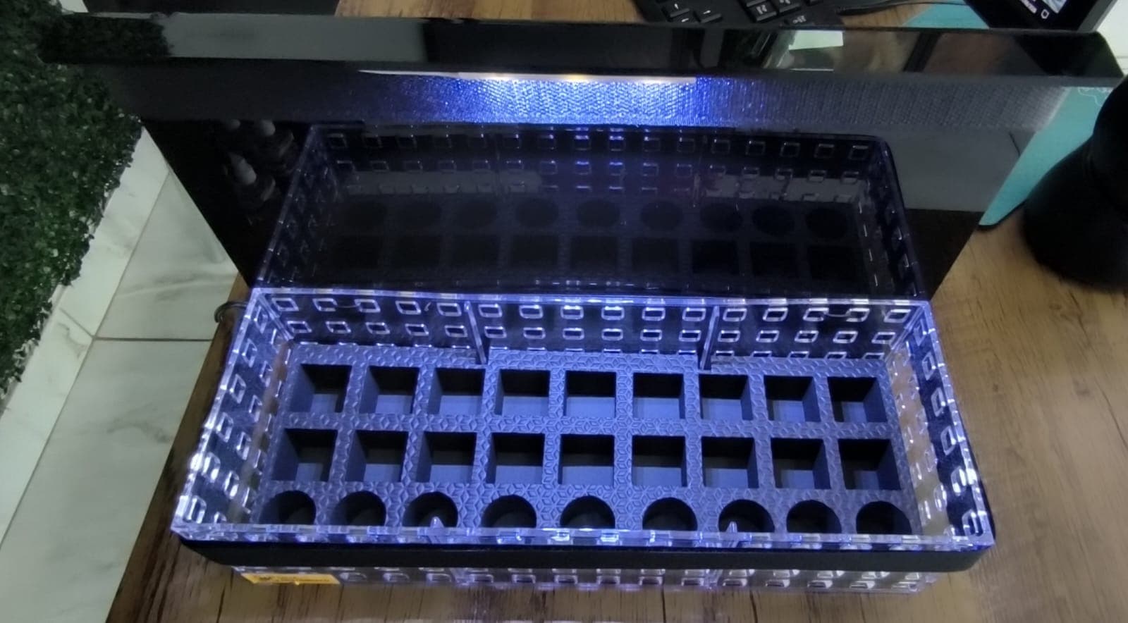 Detalhe dos compartimentos da bandeja vazia, mostrando o formato de cada encaixe e a fita de LED que ilumina os frascos.